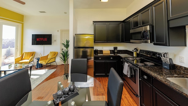A modern kitchen with dark cabinets, a stainless steel refrigerator, and a flat-screen TV mounted on the wall. - Modern King bed Haven/Free parking, Pool, Balcony (Santa Rosa Beach)