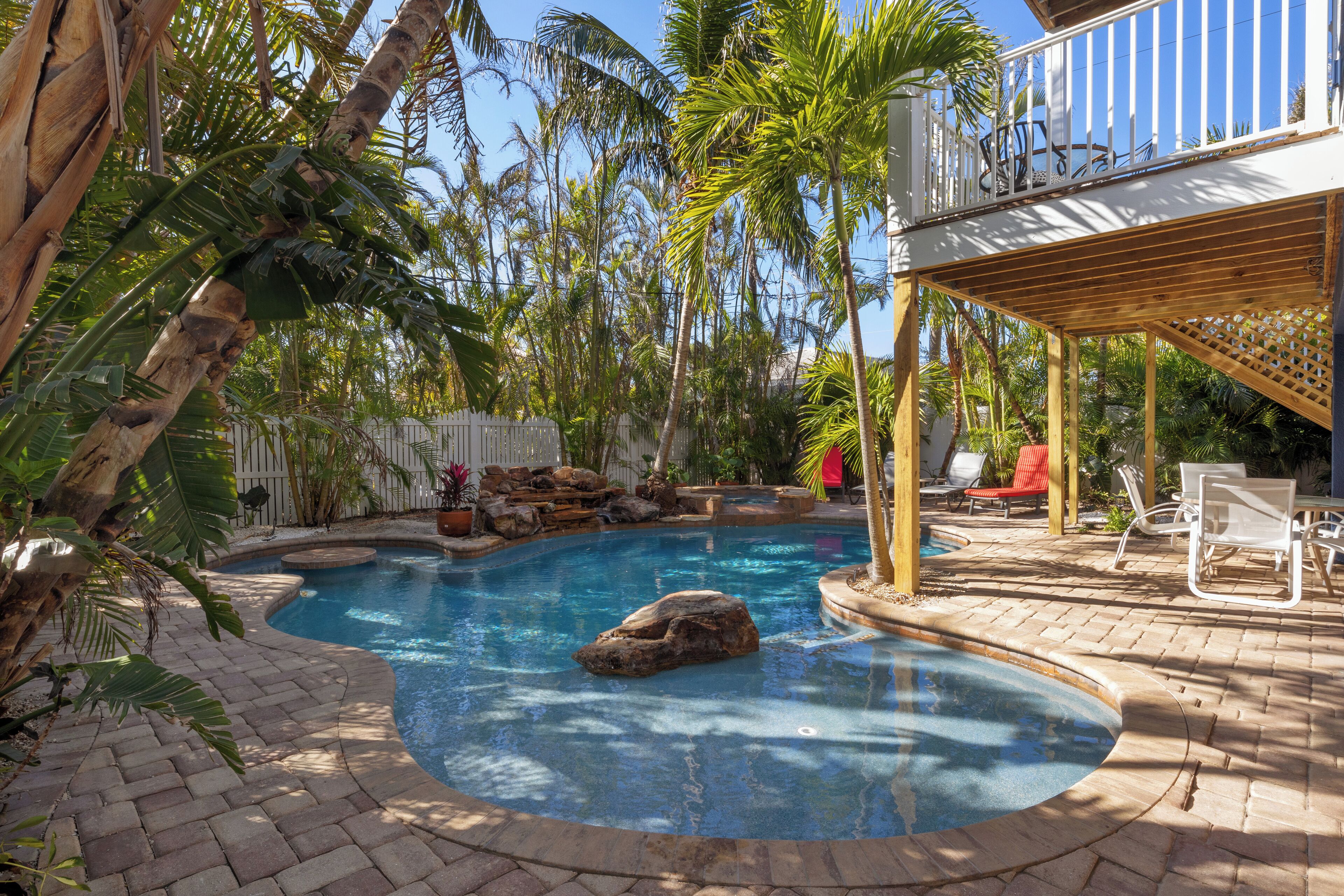 A swimming pool with a curved design, surrounded by palm trees and a wooden deck with lounge chairs.