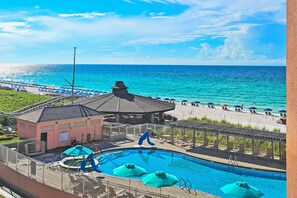 A pool area with a view of the ocean, a gazebo, and beach umbrellas.