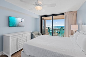 A hotel room with a bed, a TV, a desk with chairs, and a view of the ocean.