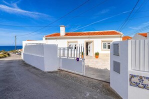 A white building with a red-tiled roof, a gated entrance, and a sign indicating 'Rua da Praia Norte.' - Assenta Beach House - 2 bedroom house with patio (São Pedro da Cadeira)