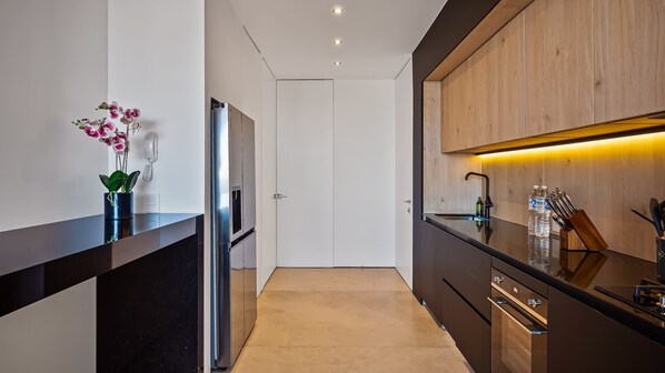 A modern kitchen with a black countertop, stainless steel appliances, wooden cabinets, and a built-in oven.