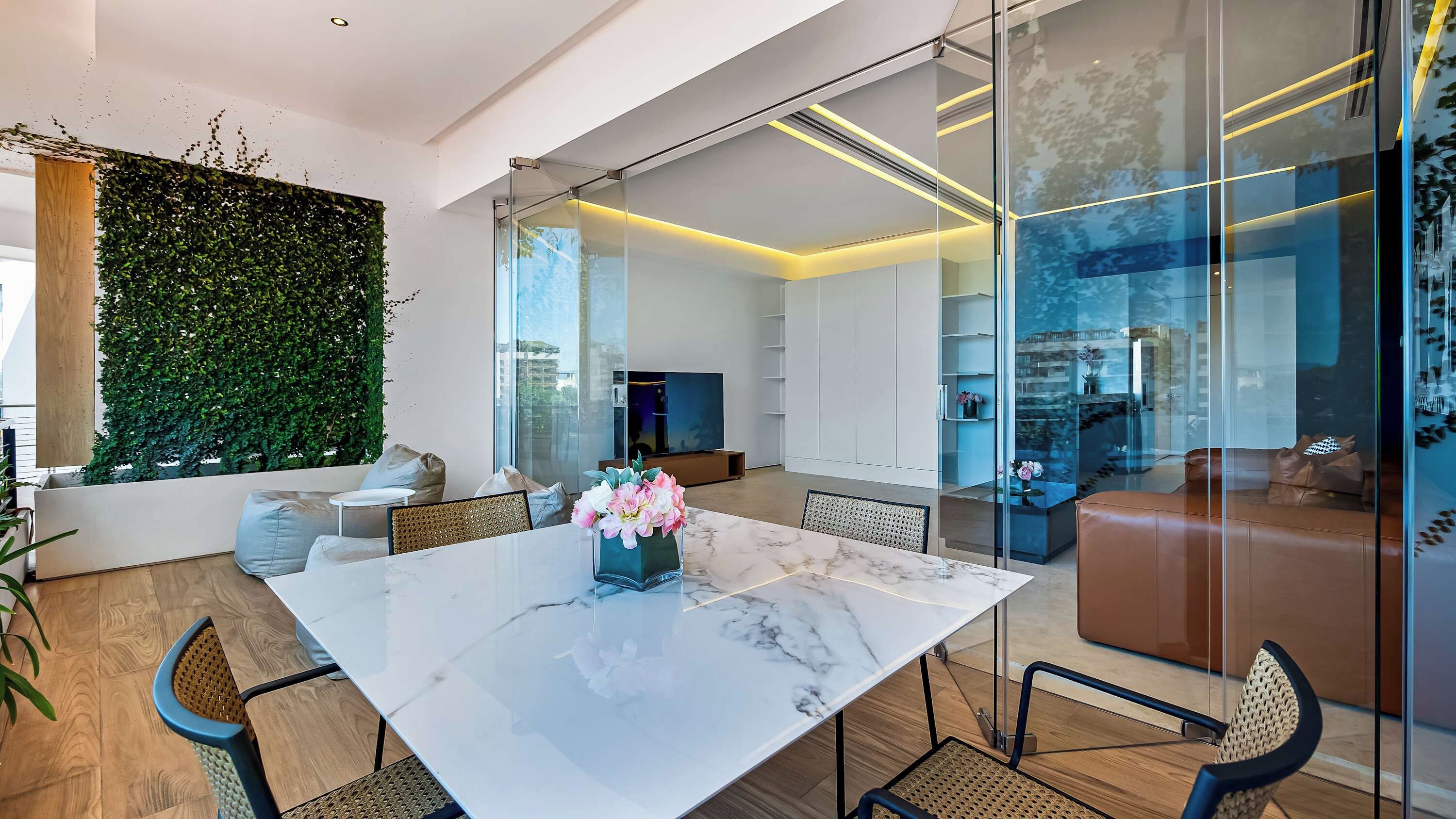 A modern living room with a marble table, comfortable seating, a large green wall, and a glass partition.