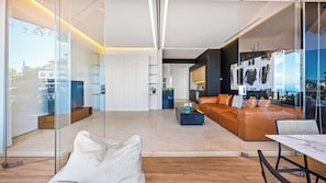 A modern living room with a glass partition, leather sofa, and a dining area with a table and chairs.