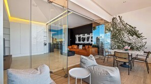 A modern living space with a glass partition, a sofa, a dining table, and a large plant.