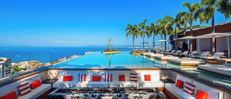 A poolside area with lounge chairs, a hot tub, and a view of the ocean.