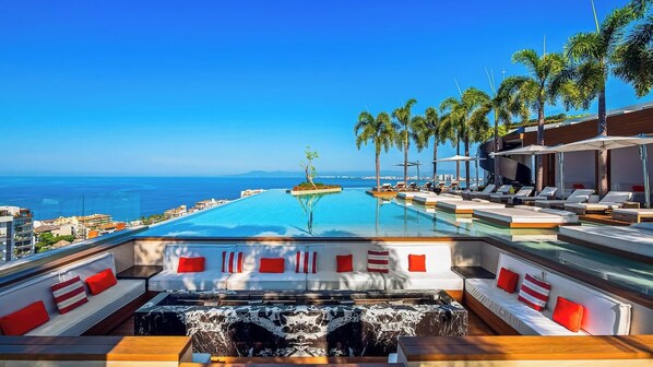 A poolside area with lounge chairs, a hot tub, and a view of the ocean.