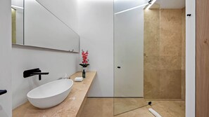 A modern bathroom with a white sink, a mirror, a shower area, and a small plant on the countertop.