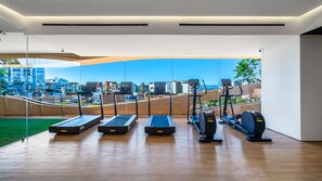 A modern gym with treadmills, elliptical machines, and a view of a cityscape.