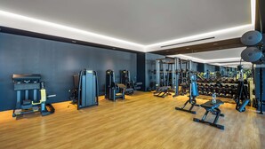 Academia moderna com diversos equipamentos de exercícios, piso de madeira e esquema de cores escuro.