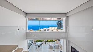 Interior moderno com uma janela ampla que oferece vista para o mar e edifícios.