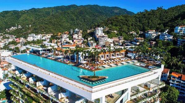 A large swimming pool with multiple lounge areas and a view of a densely built urban area with hills in the background.