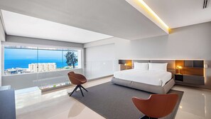 A modern hotel room with a large bed, a sitting area, and a view of the sea.