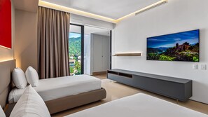 A modern hotel room with a large bed, a TV mounted on the wall, and a view of a mountainous landscape through the window.