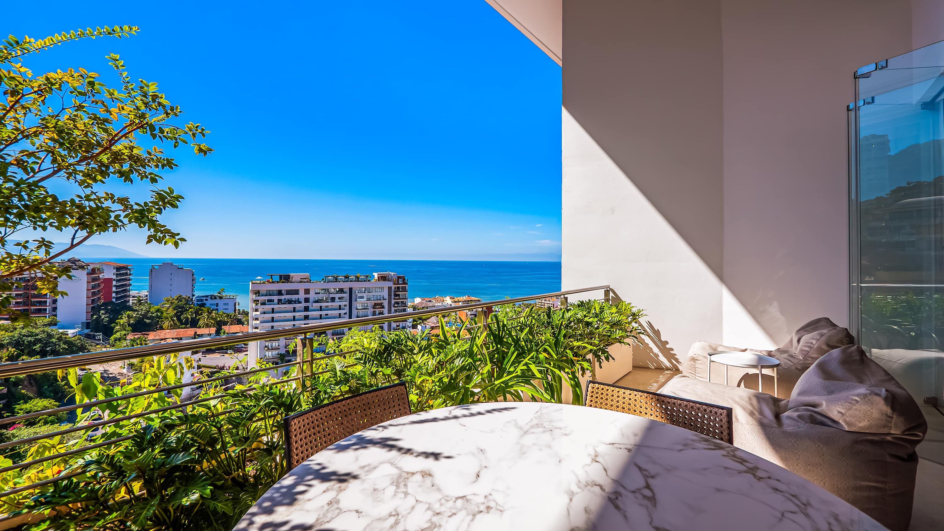 Un balcon avec vue sur la mer, une table en marbre et un canapé avec des coussins.