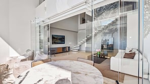 Ein modernes Interieur mit einem Marmortisch, Glaswänden und einer Treppe, die in einen oberen Bereich führt.