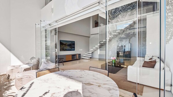 A modern interior with a marble table, glass walls, and a staircase leading to an upper level.