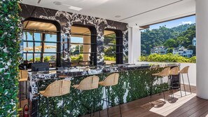 A bar area with a marble countertop, wicker chairs, and a view of a mountainous landscape.