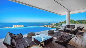 Una terraza en la azotea con vistas al mar y al paisaje urbano, amueblada con sillas de mimbre y una mesa de centro de mármol.