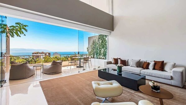 Una sala de estar moderna con un gran ventanal que da a una vista panorámica, un conjunto de sofás y una mesa de centro.