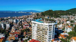 Un hotel de gran altura con varios pisos, una piscina en la azotea y vistas a la ciudad y al mar.