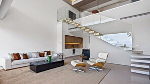 Un salon moderne comprenant un canapé, une table basse et des fauteuils, un coin cuisine et un escalier menant à un niveau supérieur.