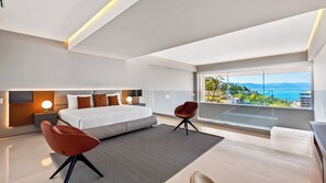A modern bedroom with a large bed, two chairs, a view of the sea, and a balcony.
