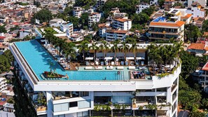 A modern hotel with a rooftop infinity pool, surrounded by palm trees and offering views of the cityscape.