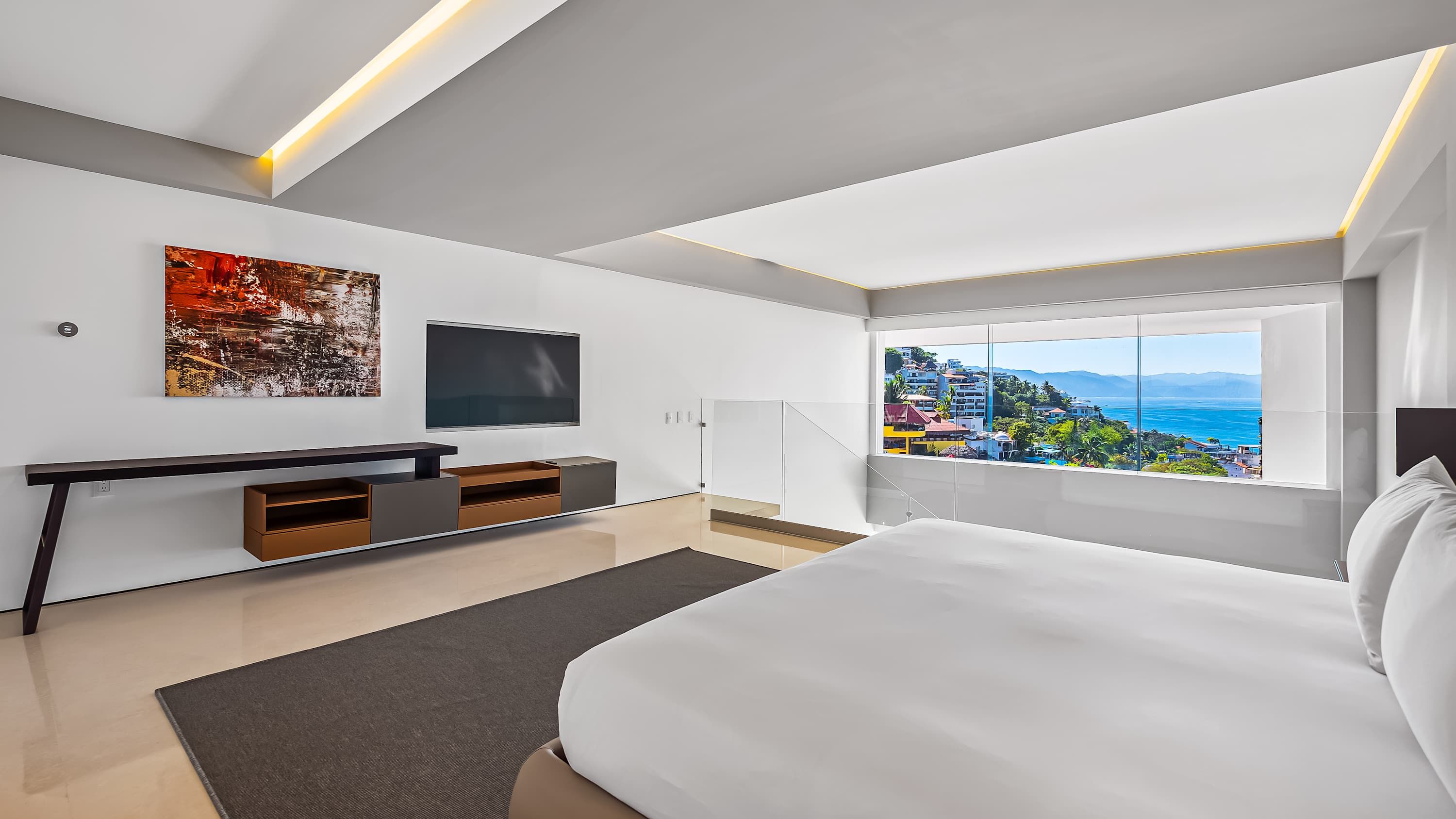 Une chambre moderne avec un grand lit, une télévision, une console et une vue sur la ville.