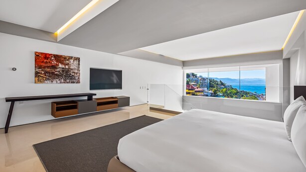 Ein modernes Schlafzimmer mit einem großen Bett, einem Fernseher, einem Konsolentisch und Blick auf die Stadt.