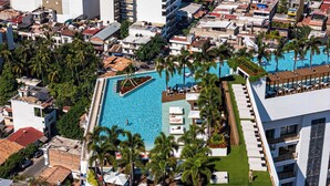 Luftaufnahme eines Resorts mit einem zentralen Swimmingpool, umgeben von Palmen und Liegebereichen.