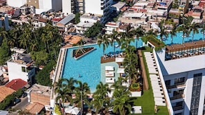 Luftaufnahme eines Resorts mit einem zentralen Swimmingpool, umgeben von Palmen und Liegebereichen.