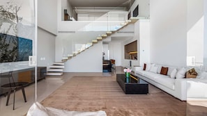 A modern interior with a staircase leading to an upper level, a white sofa, a coffee table, and a glass wall with a view. - SoHo PV - PH 11 (Puerto Vallarta)