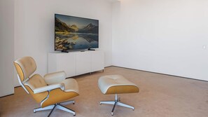 A modern living room with a flat-screen TV mounted on a white cabinet, a beige leather armchair, and a matching ottoman. - AlilaHolidays - Luxury Getaway in SOHO PV - 105 (Puerto Vallarta)