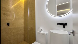 A modern bathroom with a glass shower enclosure, a white sink, and a mirror with integrated lighting.
