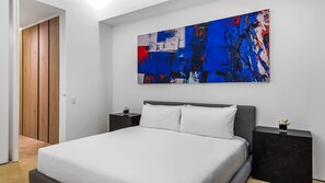 A modern bedroom with a large bed, a nightstand, a bedside table, and a colorful abstract painting on the wall.