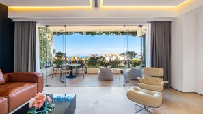 Una sala de estar moderna con un sofá de cuero, una mesa de comedor de vidrio y vistas a un paisaje urbano a través de ventanas amplias.