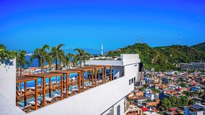 Un hotel con piscina en la azotea, vistas de la ciudad y una colina con una aguja de iglesia.
