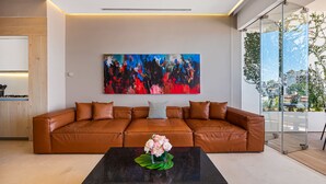 A modern living room with a brown leather sofa, a black coffee table with a floral centerpiece, and a large abstract painting on the wall. - SoHo PV - 411 (Puerto Vallarta)
