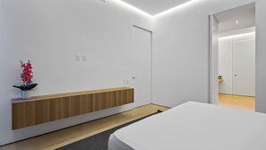Un dormitorio moderno con una mesita de noche de madera, una cama blanca y una planta en maceta.