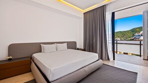 A modern hotel room with a large bed, a nightstand, a small table with a flower, and a view of a balcony and buildings.