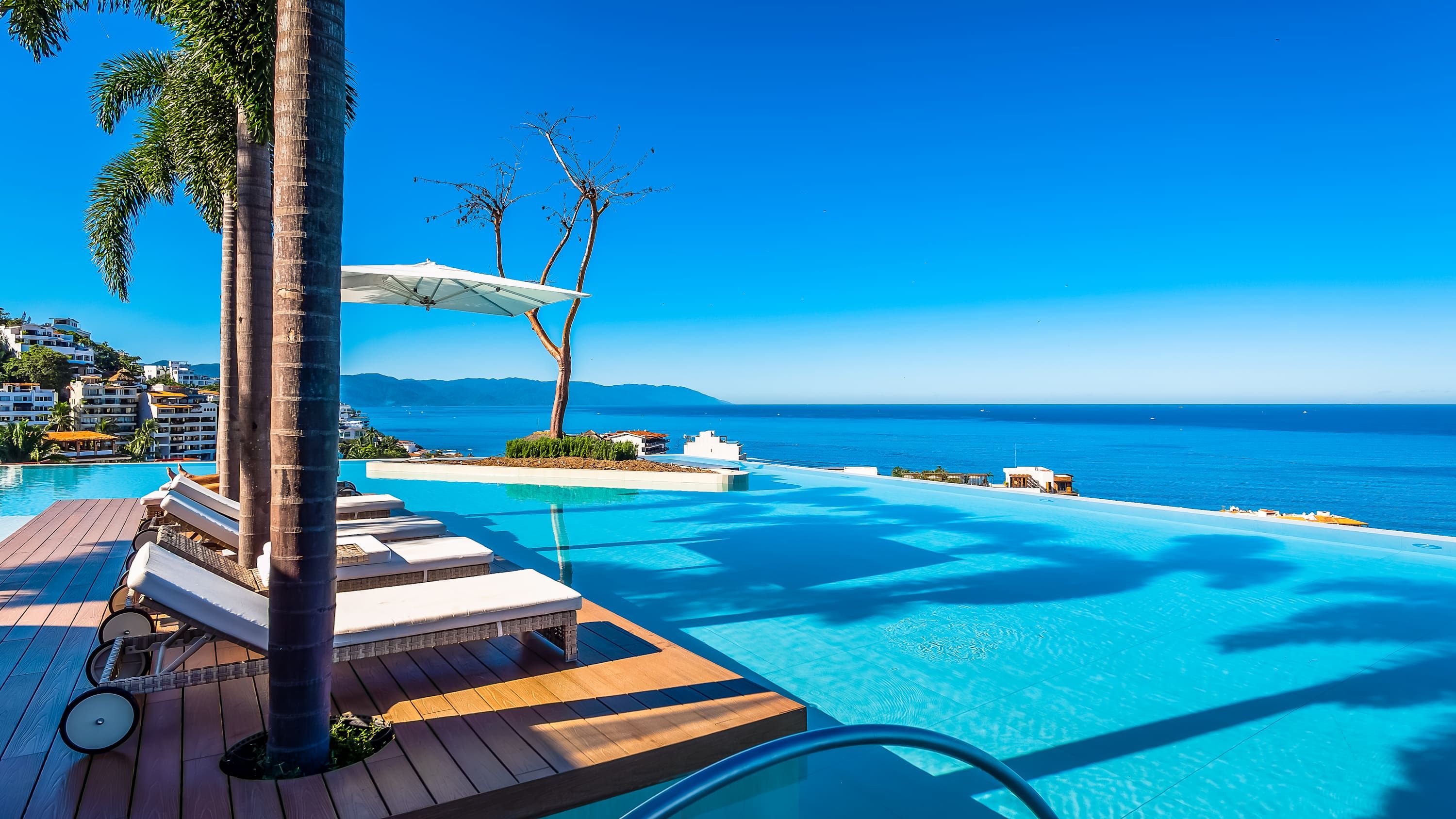 Céu azul límpido, piscina com espreguiçadeiras e vista para o mar.