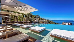 An infinity pool with lounge chairs and umbrellas, overlooking a coastal town.