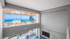 A modern apartment with a large balcony, a view of the sea, and a cityscape.