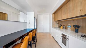 Eine moderne Küche mit dunkler Arbeitsplatte, weißen Schränken und einer Holzrückwand. Am Tresen stehen zwei orangefarbene Stühle und ein Spülbecken mit Armatur.