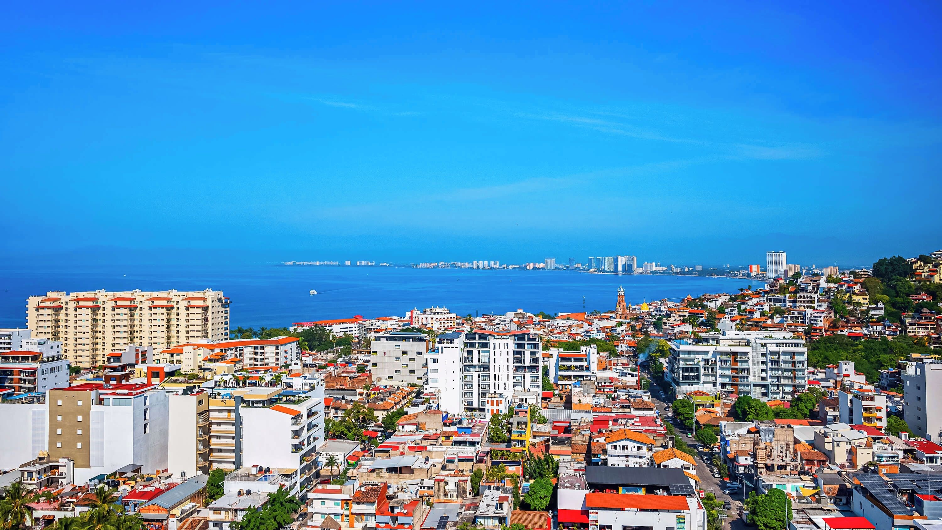 Un paisaje urbano costero con una construcción densa, una torre destacada y una vista despejada del mar.