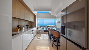 Une cuisine moderne avec des meubles blancs, un grand îlot central et une vue sur l’océan.