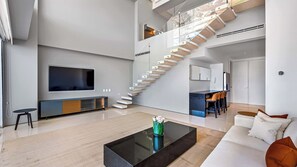Ein modernes Wohnzimmer mit Flachbildfernseher, Couchtisch und einer Treppe, die in eine obere Etage führt.