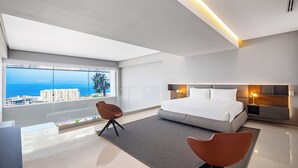 A modern hotel room with a large bed, a sitting area, and a view of the sea.