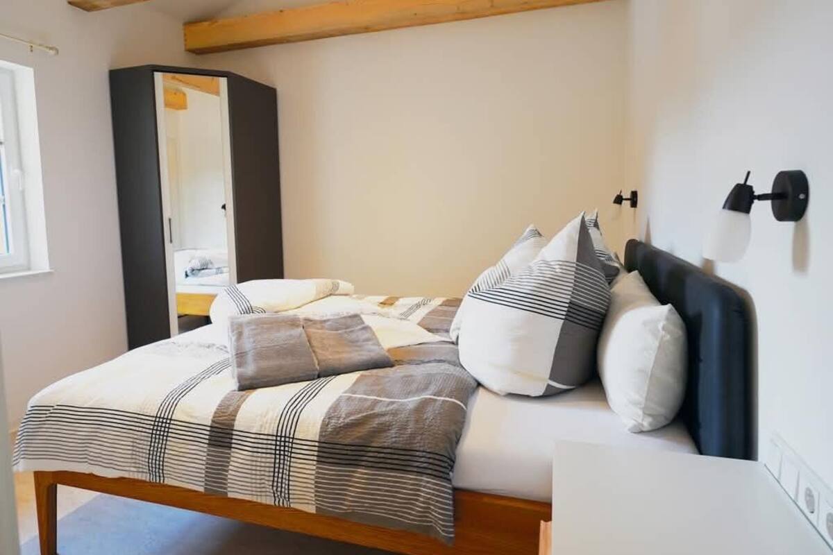 Un dormitorio con cama, almohadas, un armario y una lámpara fijada a la pared.